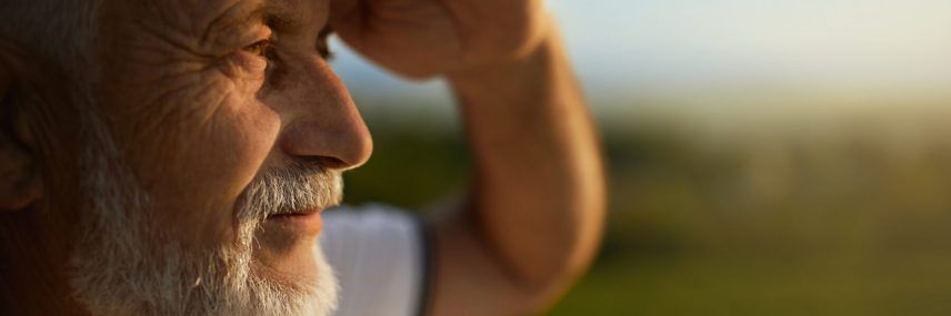 Bearded man squinting from bright sun, while looking into distance during trip.